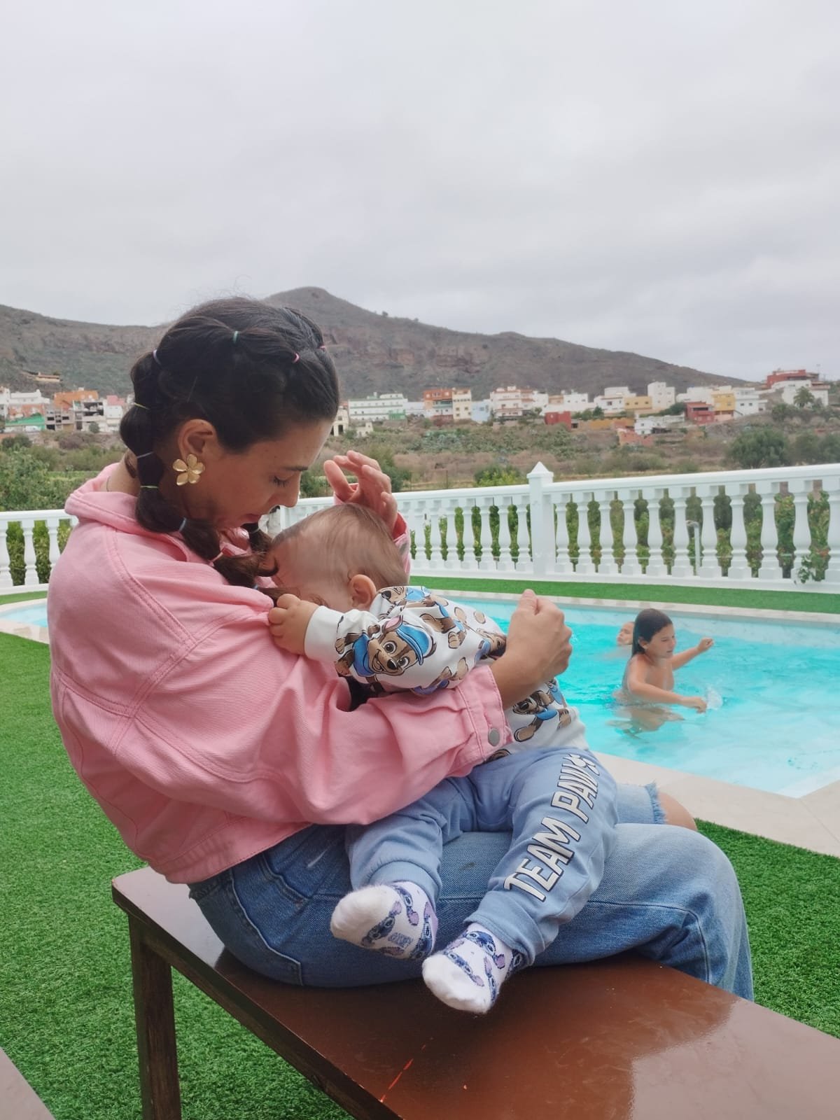 Mamá abrazando y amamantando a su bebé de 19 meses junto a la piscina, en un día nublado, transmitiendo ternura, conexión y amor incondicional.