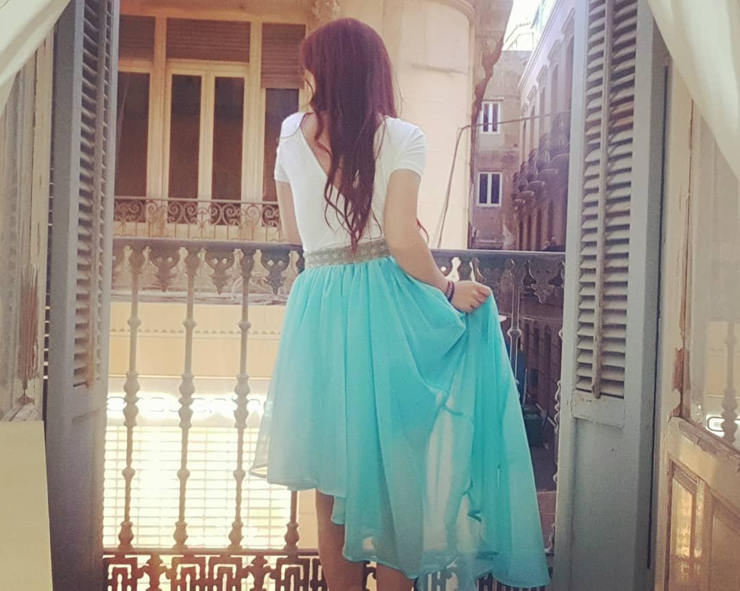 Mamá Zombi Chic de espaldas en un balcón, con una falda azul vaporosa, representando su historia íntima en la sección Lo que Nunca Conté.