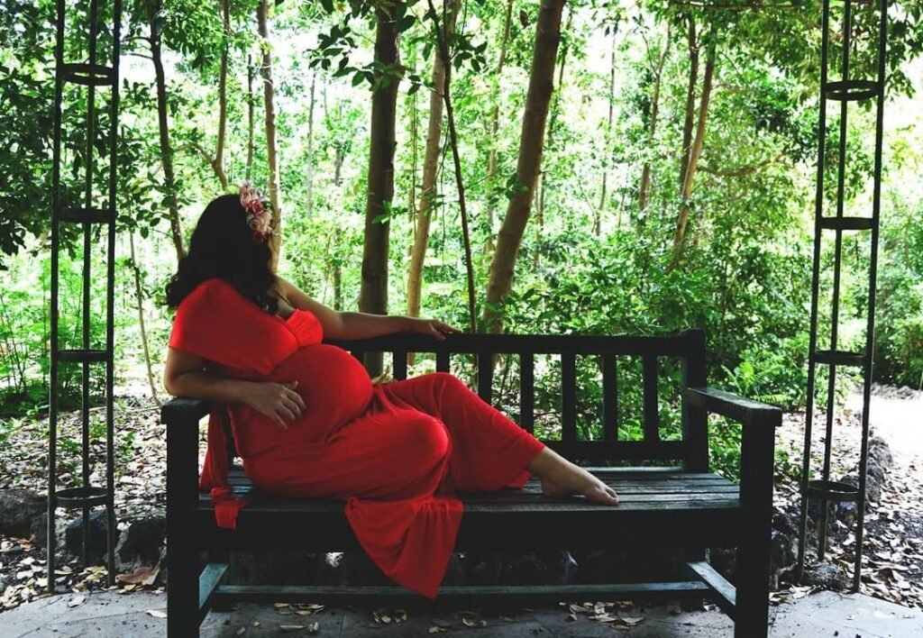 Mamá Zombi Chic embarazada de su primera hija, sentada en un banco en la naturaleza. Fotografía profesional en un bosque, maternidad real y emocional.